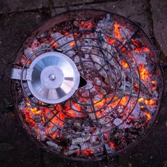 Kettle warming over glowing campfire coals