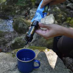 Filtering water into a camp mug by a stream